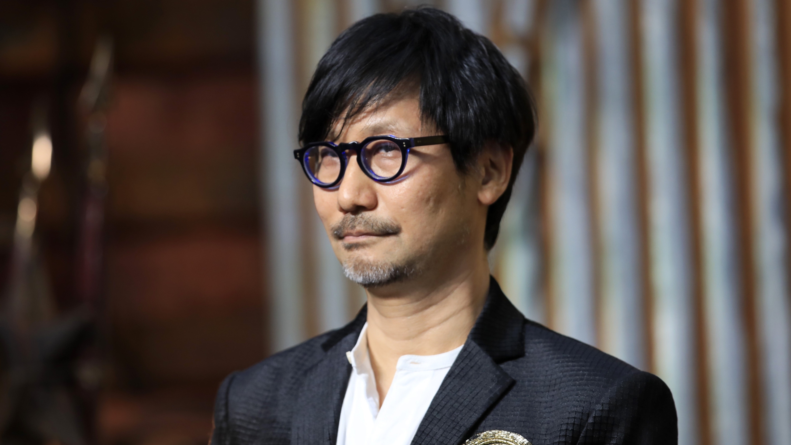 Hideo Kojima'nın 10. Yıldönümü Etkinliği ve Projeler 1 Hideo Kojima presenting at the 10th anniversary event of Kojima Productions in Tokyo, with a futuristic and vibrant atmosphere.