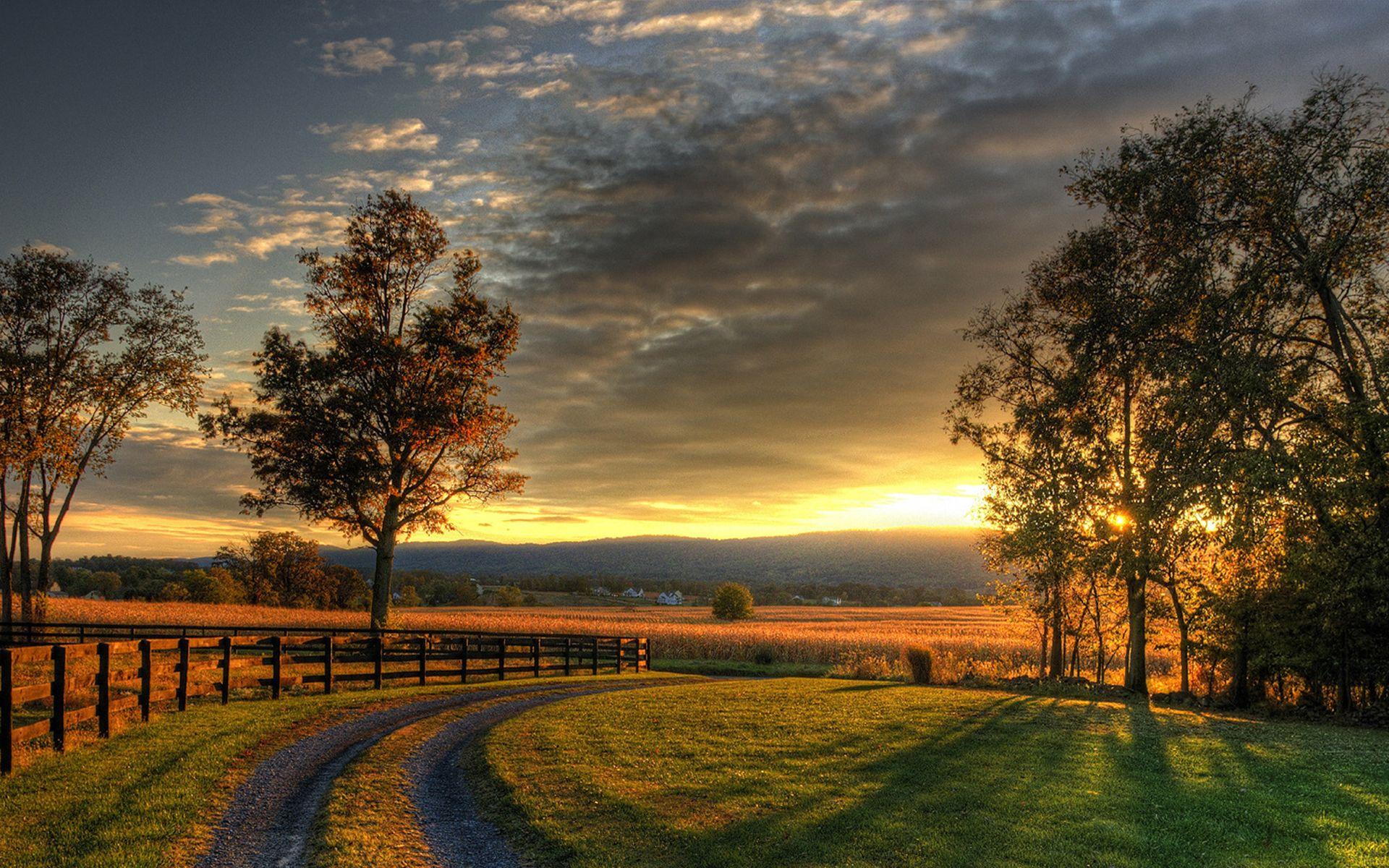 A peaceful countryside landscape at sunset with rolling hills and a quaint farmhouse.